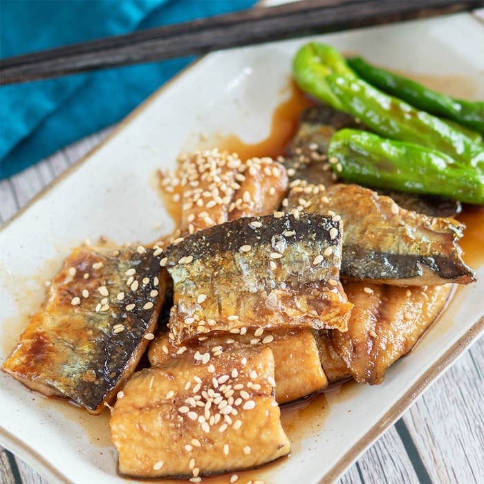 焼き魚の切り身が皿に盛られ、ゴマがトッピングされている。隣には焼き唐辛子が添えられている。