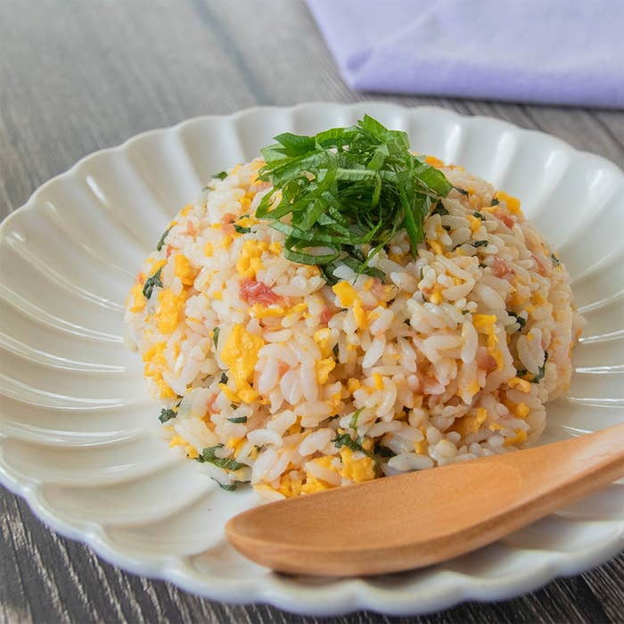 皿に盛られた梅と大葉のチャーハン。卵や刻んだ野菜が混ざり、大葉がトッピングされている。横に木のスプーンが置かれている。