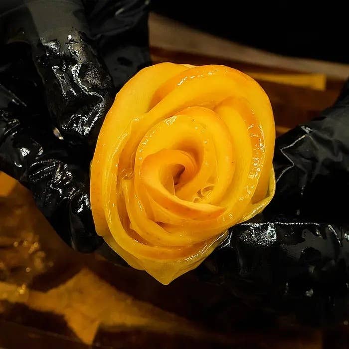 手袋をした手が、彫刻されたバラの形をした野菜を持っている。
