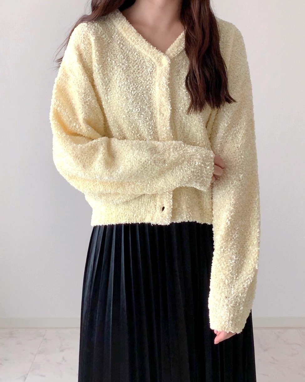 女性がふんわりした生地のカーディガンとプリーツスカートを着用している。