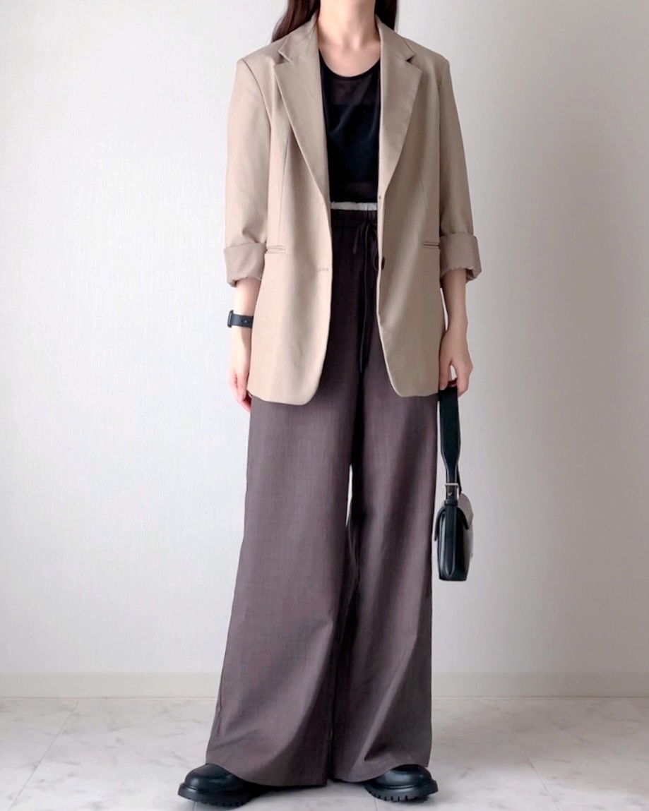 女性がゆったりしたパンツとブレザーを着用し、小さなバッグを持ってポーズをとっています。カジュアルシックなスタイル。