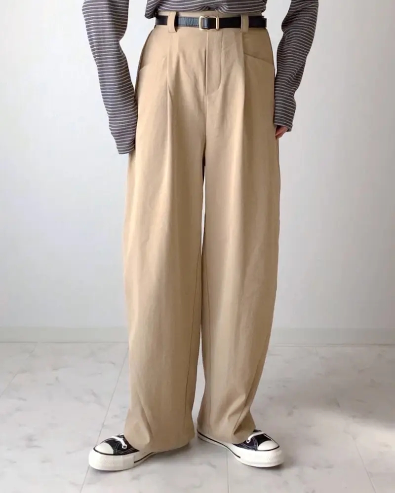 ゆったりとしたベージュのワイドパンツとストライプの長袖を着た人物の下半身。スニーカーを履いている。