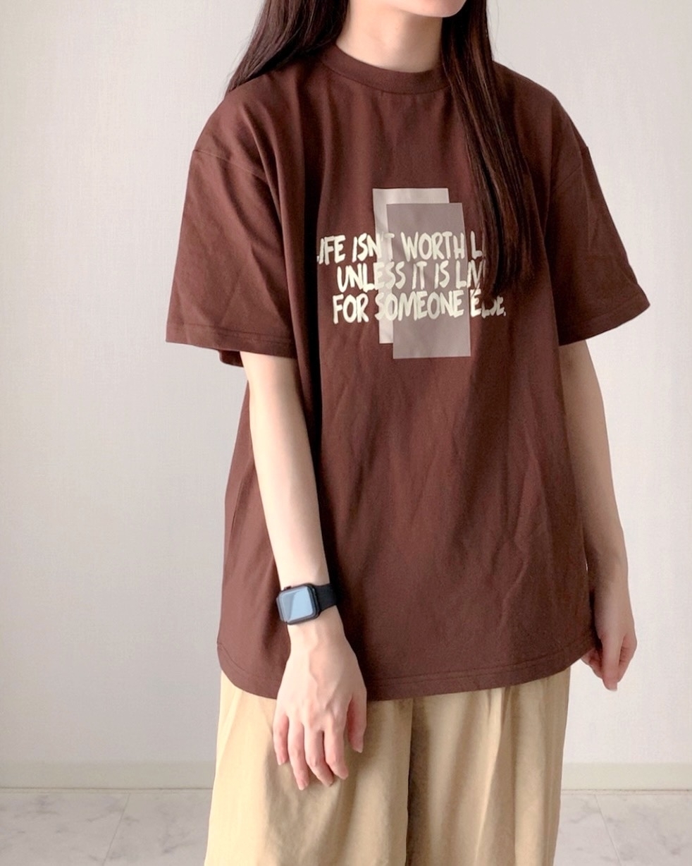 女性がプリントTシャツとパンツを着用している。時計をつけている。