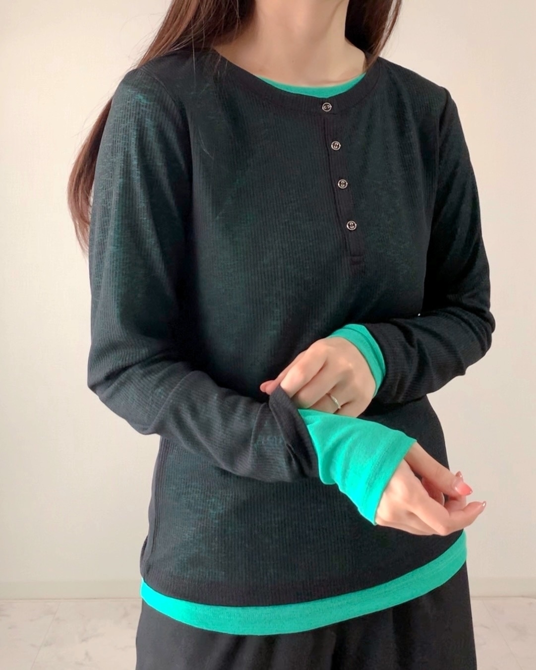 女性が長袖シャツの袖を引っ張っている。シンプルなデザインのカジュアルな服装。
