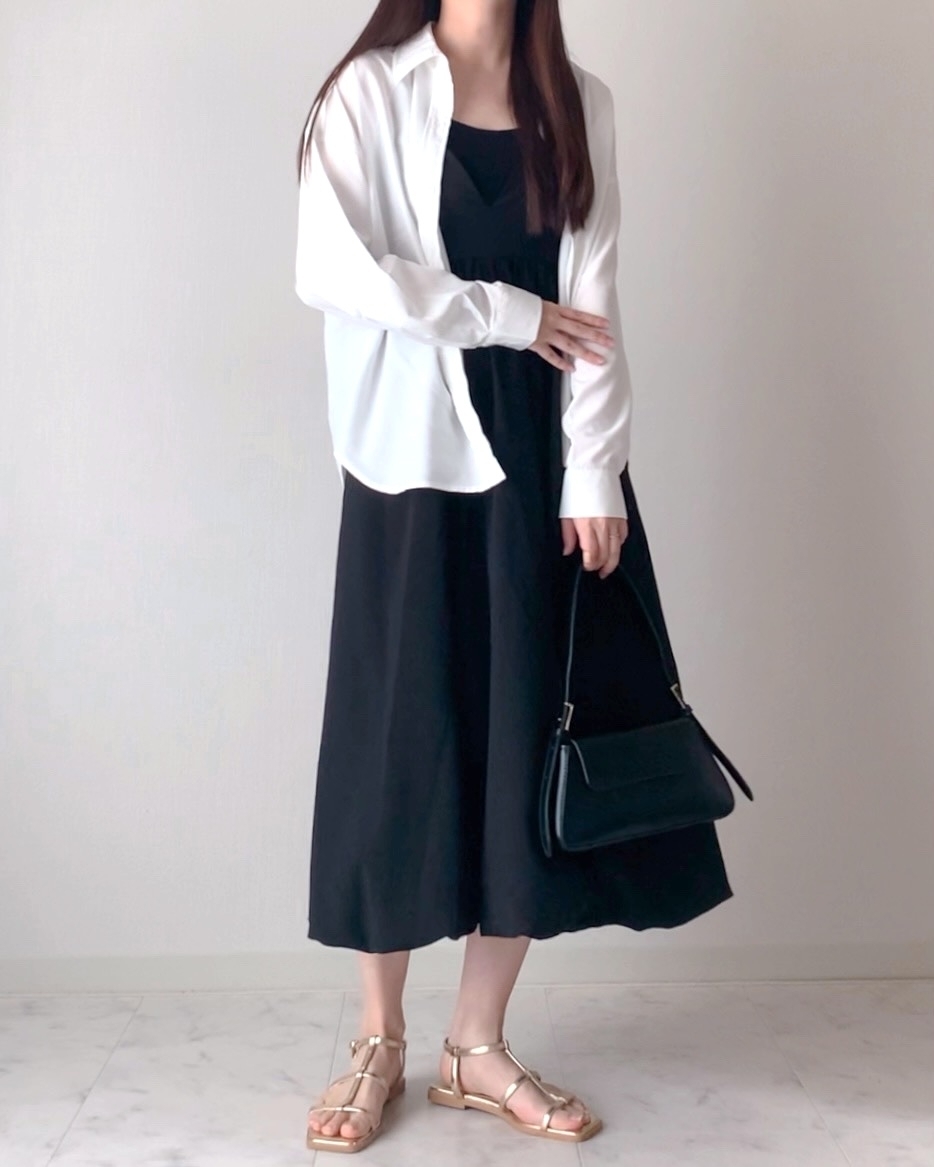 女性が黒のロングドレスに白いシャツを羽織り、サンダルを履き、バッグを持っている。カジュアルでシンプルなスタイル。