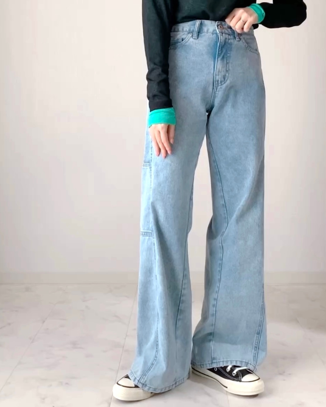 ゆったりしたデニムとスニーカーを履いた、スタイリッシュな服装をした人物の全身写真。
