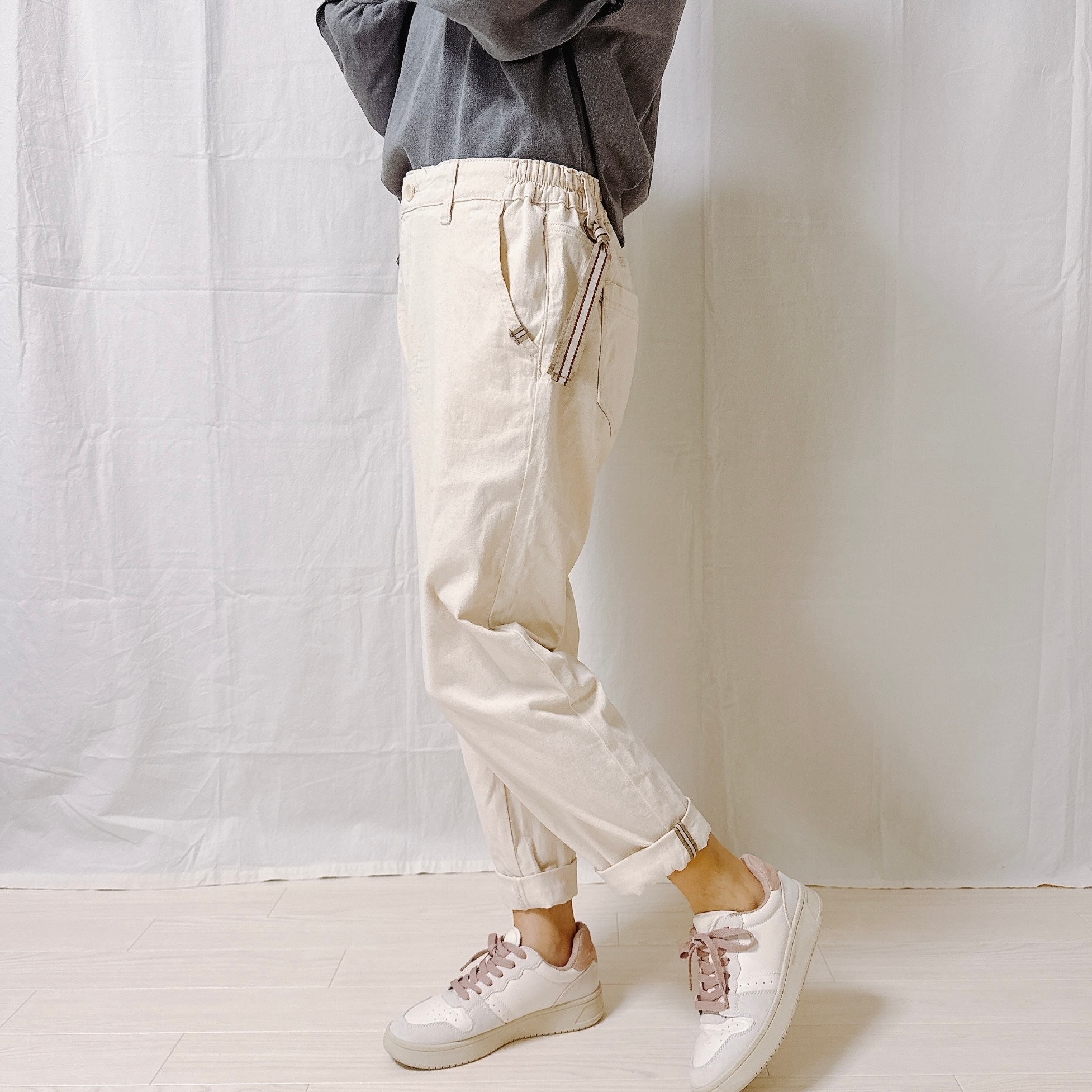 カジュアルな服装の人物が横向きに立っています。グレーのトップスとベージュのパンツ、スニーカーを着用しています。