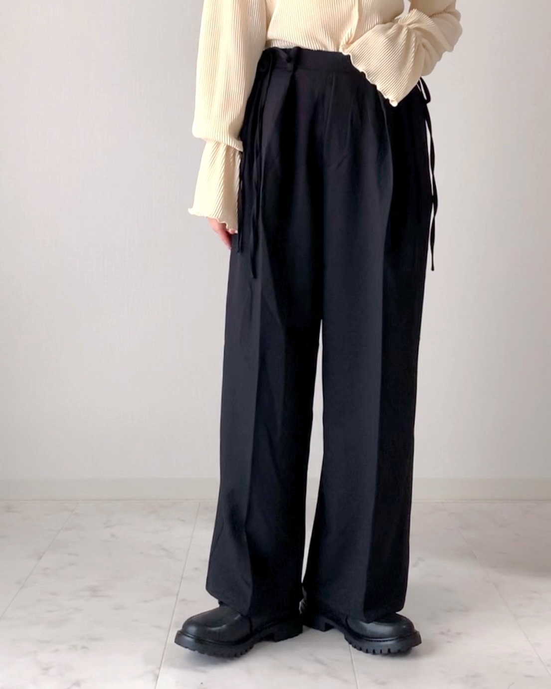 長袖トップスとワイドパンツ、ブーツを履いた人物が立っている。顔は写っていない。
