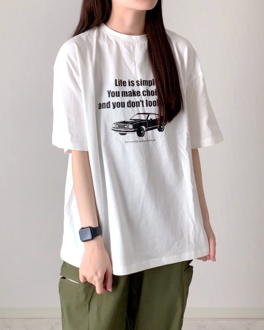 腕時計をつけた人物がメッセージTシャツを着て、シンプルなパンツスタイル。