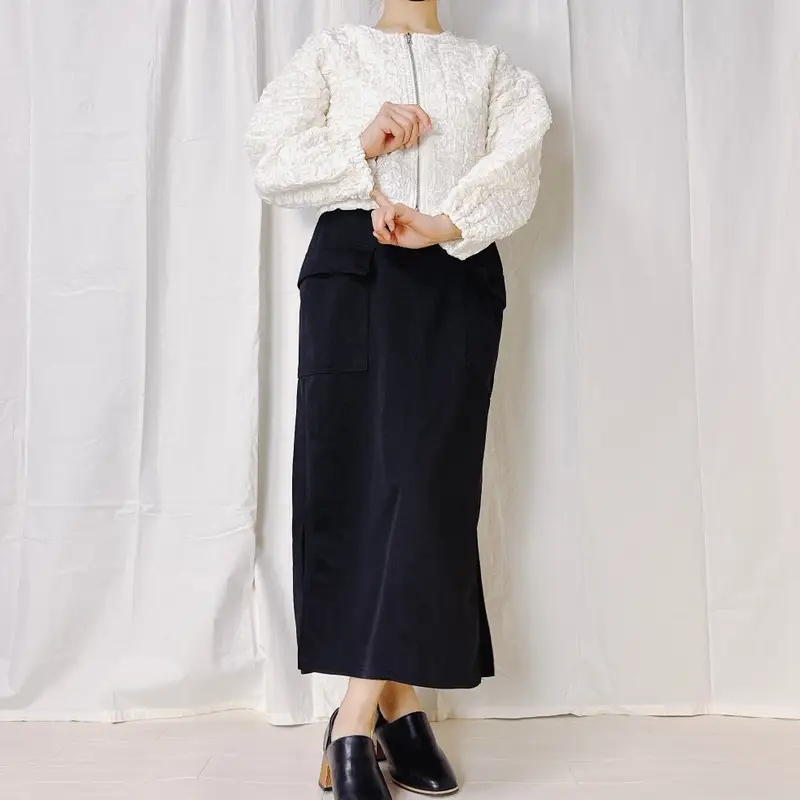 白いジャケットと黒いロングスカートを着た人物がポーズを取っています。