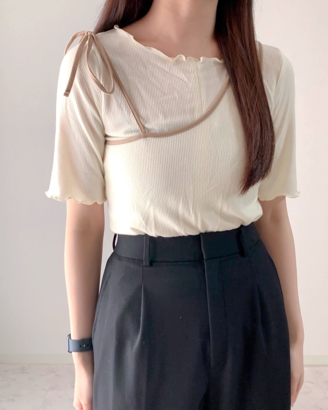 女性がリボン付きのシンプルで洗練されたトップスとハイウエストパンツを着ている。