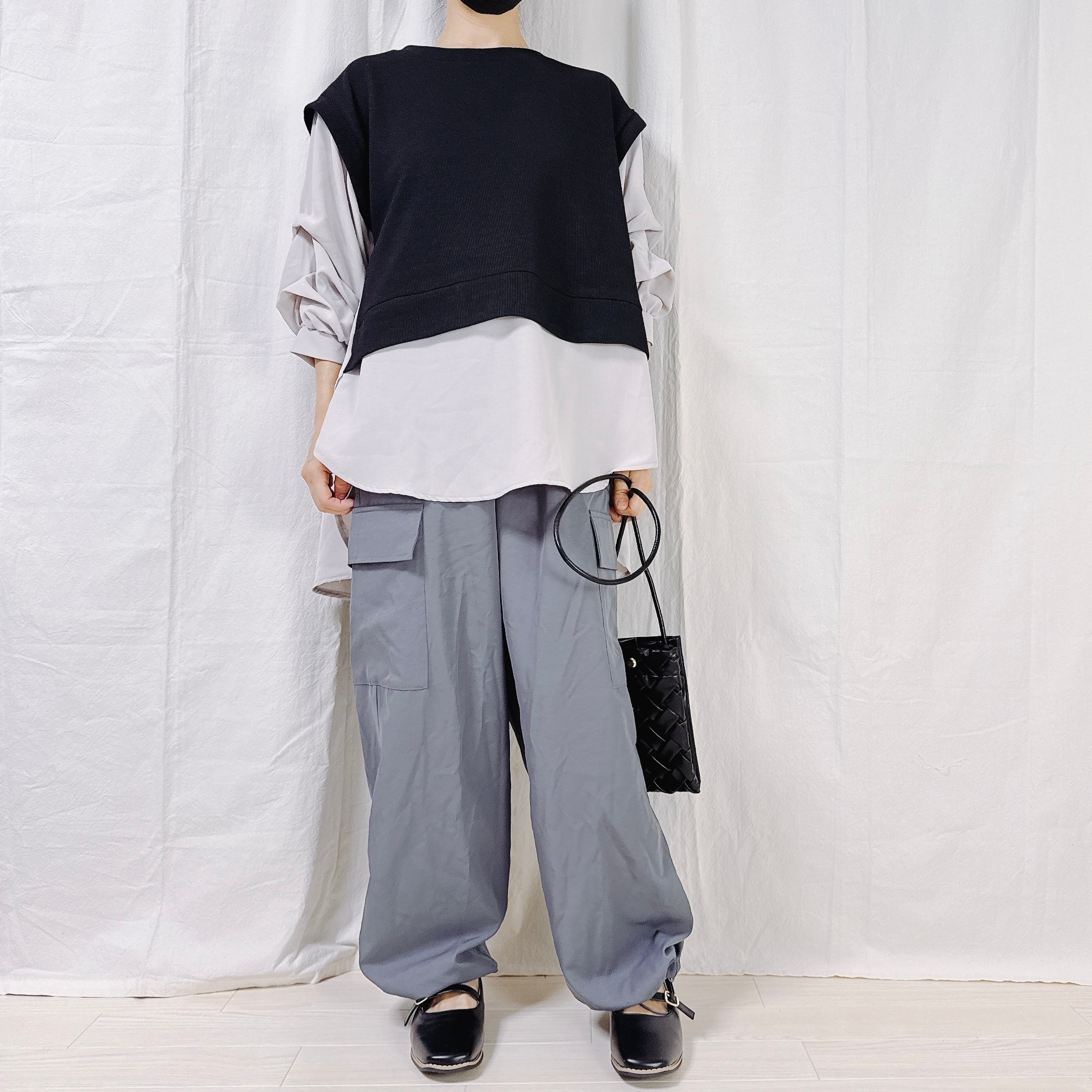 ゆったりとした白シャツと黒のベスト、カーゴパンツを着た人物が、シンプルでモダンなファッションを披露しています。