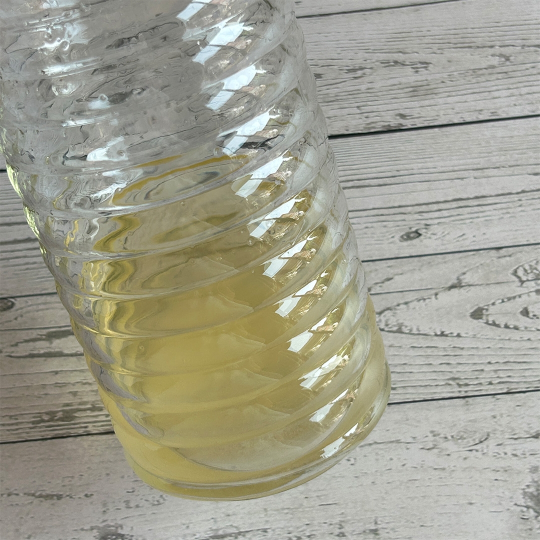 ガラスのボトルに黄色い飲み物が少量入っており、木目調のテーブルに置かれている。