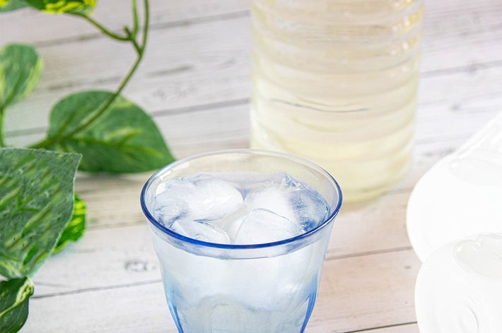 氷の入ったグラスとボトルが白い木のテーブルに置かれ、葉の装飾が周囲にある。