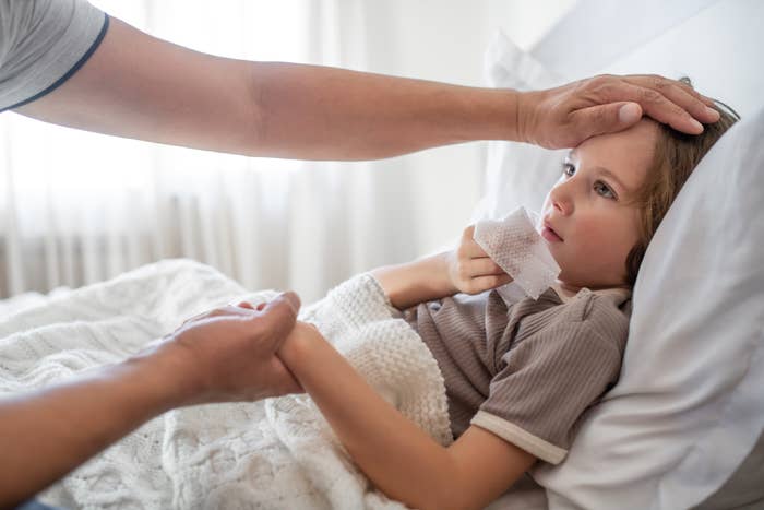 Child lying successful bed, holding a tissue, portion an big mildly feels their forehead, checking for a fever