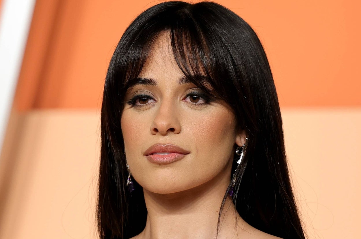 A person with long, dark hair and fringe poses for a portrait, wearing dangling earrings