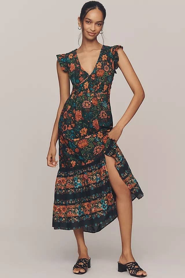 Model wearing a floral-patterned, bohemian-style dress with a slit and ruffled sleeves, paired with strappy sandals