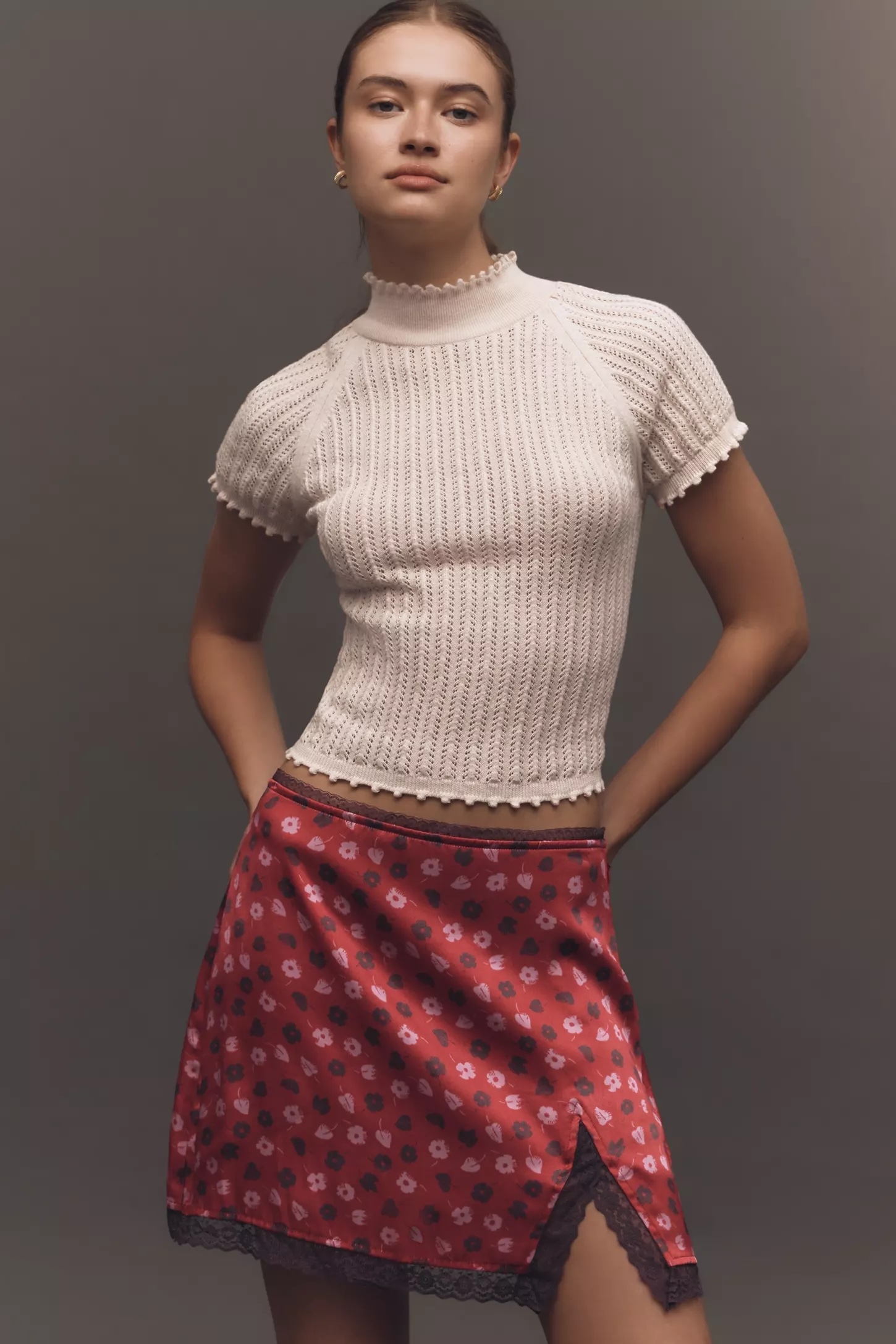 Model wearing a fitted knit top and a floral-patterned skirt with a lace hem, hands in pockets, posing for a fashion article