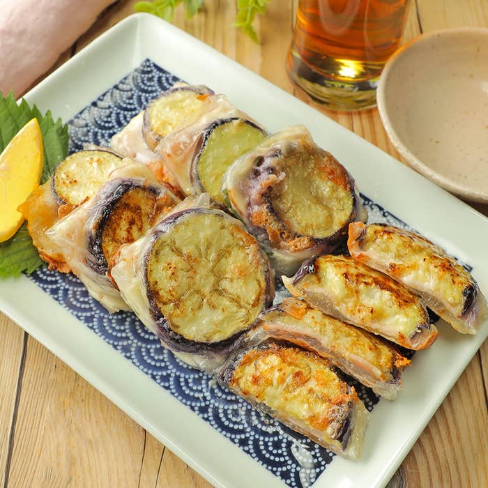 焼きナスの輪切りを生春巻きの皮で包んで焼いた料理が皿に並べられています。そばには飲み物があります。