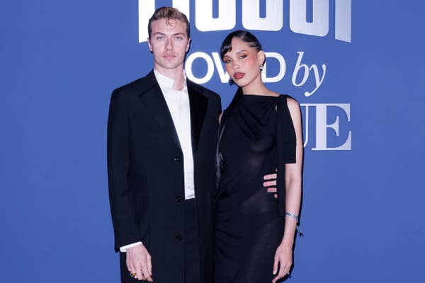 Lucky Blue Smith and Nara Smith posing together at an event, dressed in stylish formal attire. A logo is visible in the background