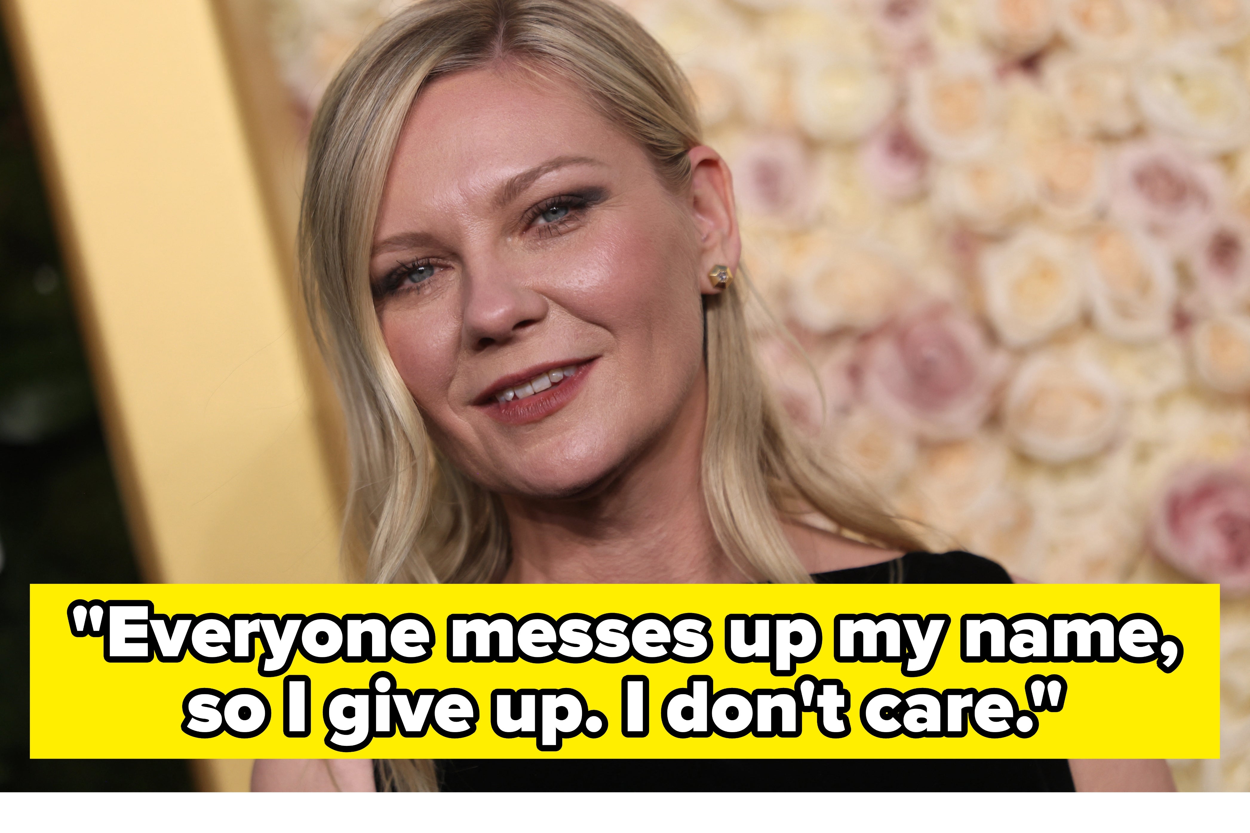 Kirsten Dunst with long hair smiles in front of a floral backdrop, wearing a sleeveless top