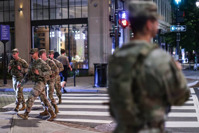 Military unit successful azygous crossing a metropolis thoroughfare astatine night, with 1 worker lasting successful the foreground