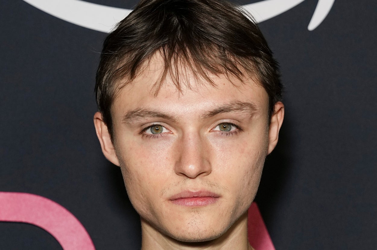 Mingus Reedes in a simple t-shirt at a media event, standing against a backdrop with a partial logo visible