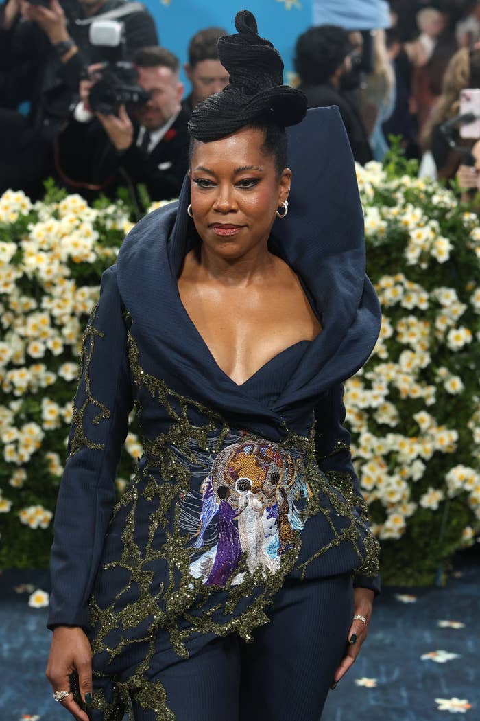 Regina King connected a reddish carpet successful a stylish heavy neckline gown with intricate embroidery, surrounded by flowers and photographers successful the background
