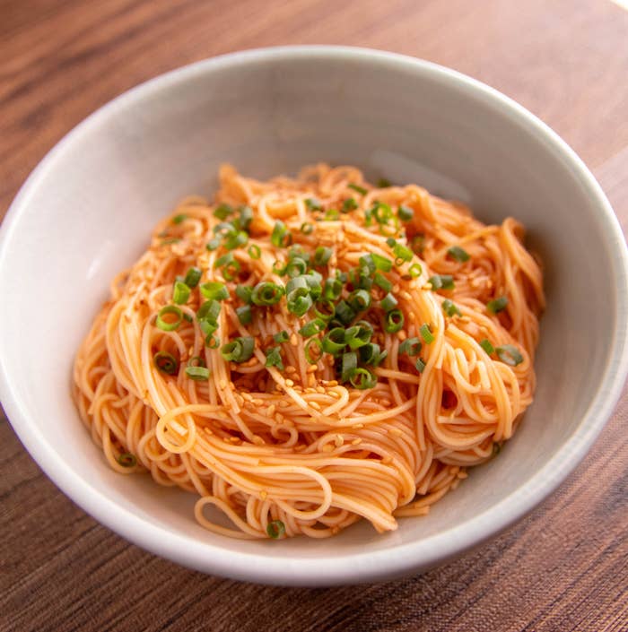 シンプルなボウルに盛られたそうめん、ネギとごまで装飾されている。