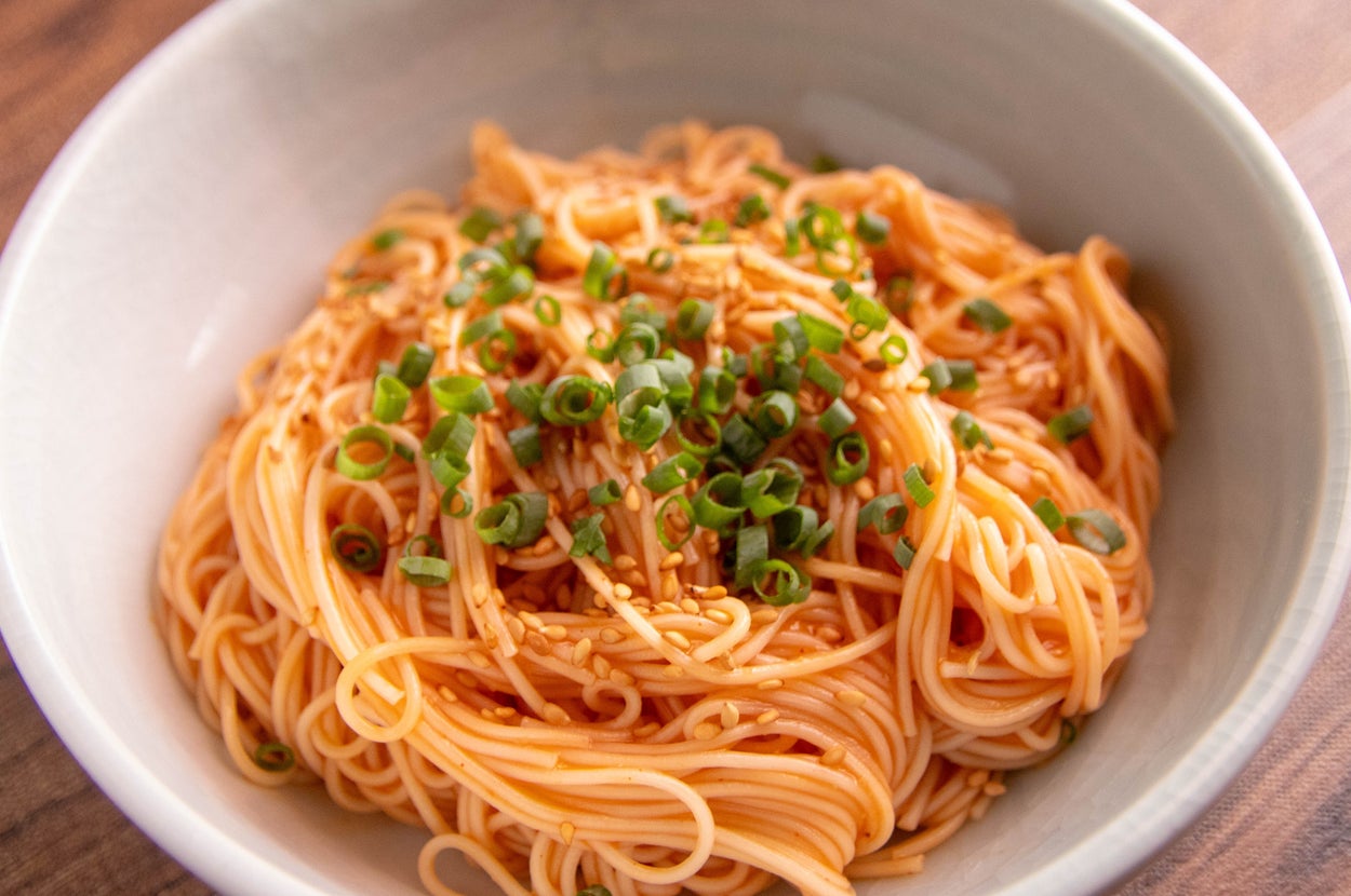 白いボウルに、ネギとゴマがトッピングされたアジアンスタイルの麺料理が盛られています。