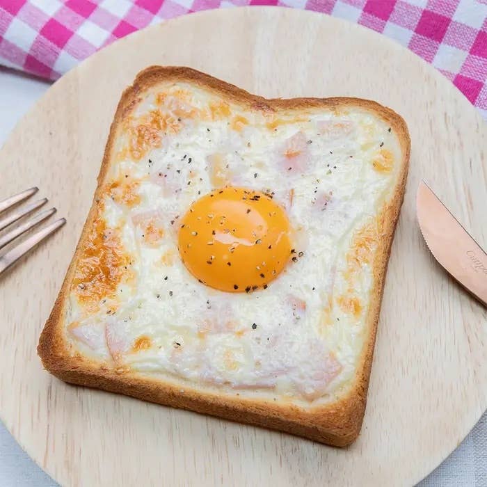 トーストの上に目玉焼きとチーズがのった料理が木製のプレートに載っています。