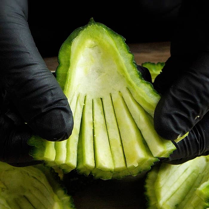手袋をした手が、細かく切り込みを入れた緑色の野菜を持っている様子。