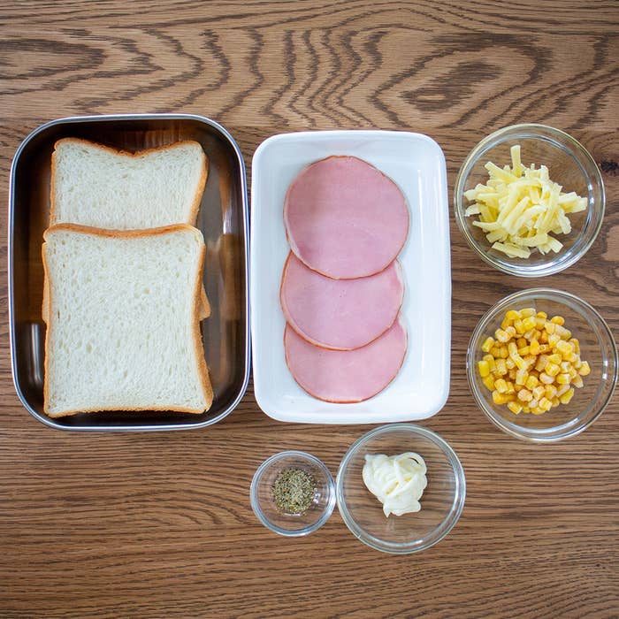 食パン、ハム、チーズ、コーン、マヨネーズ、胡椒が木製テーブルの上に並んでいる。