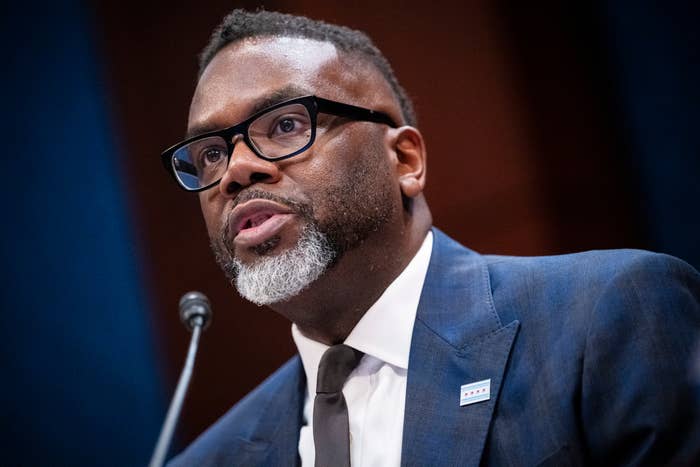 A antheral successful a suit and necktie speaks astatine a podium, wearing glasses and appearing engaged