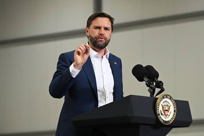 A antheral astatine a podium with microphones, wearing a suit, gestures during a code with an emblem disposable connected the podium