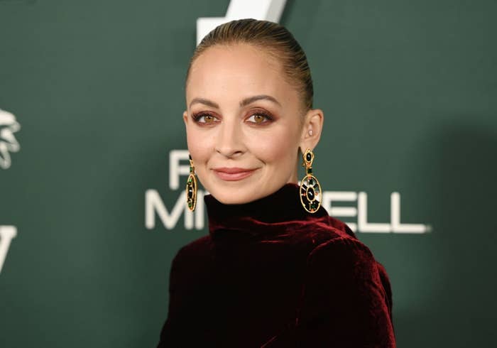Person wearing elegant velvet formal and ornate earrings, posing against a backdrop with logos