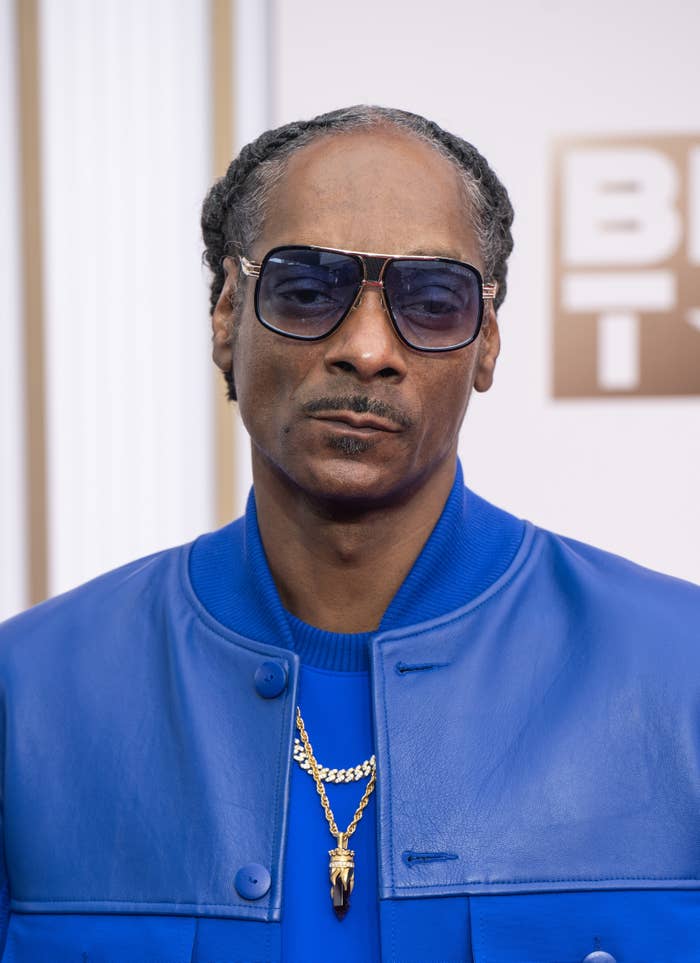 Snoop Dogg wearing blue jacket and sunglasses, accessorized with a gold necklace