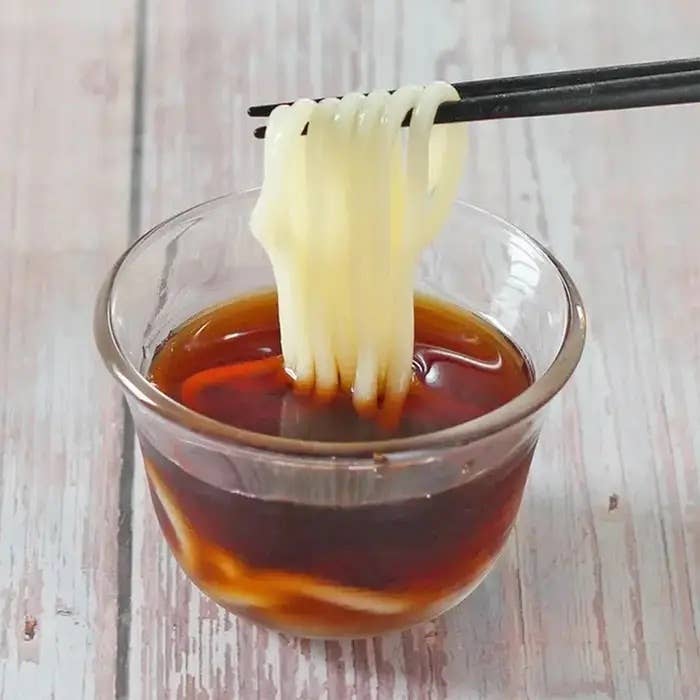 ガラスの器に入った麺つゆに、箸でつまんだ素麺が入っている様子。