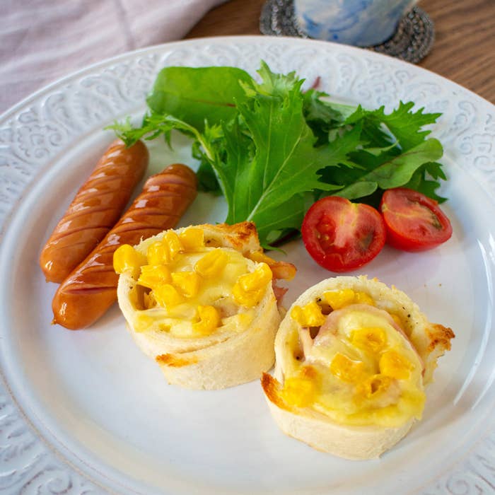 皿にサラダ、ソーセージ、トマト、コーンの乗ったパンロールが盛られた朝食プレート。