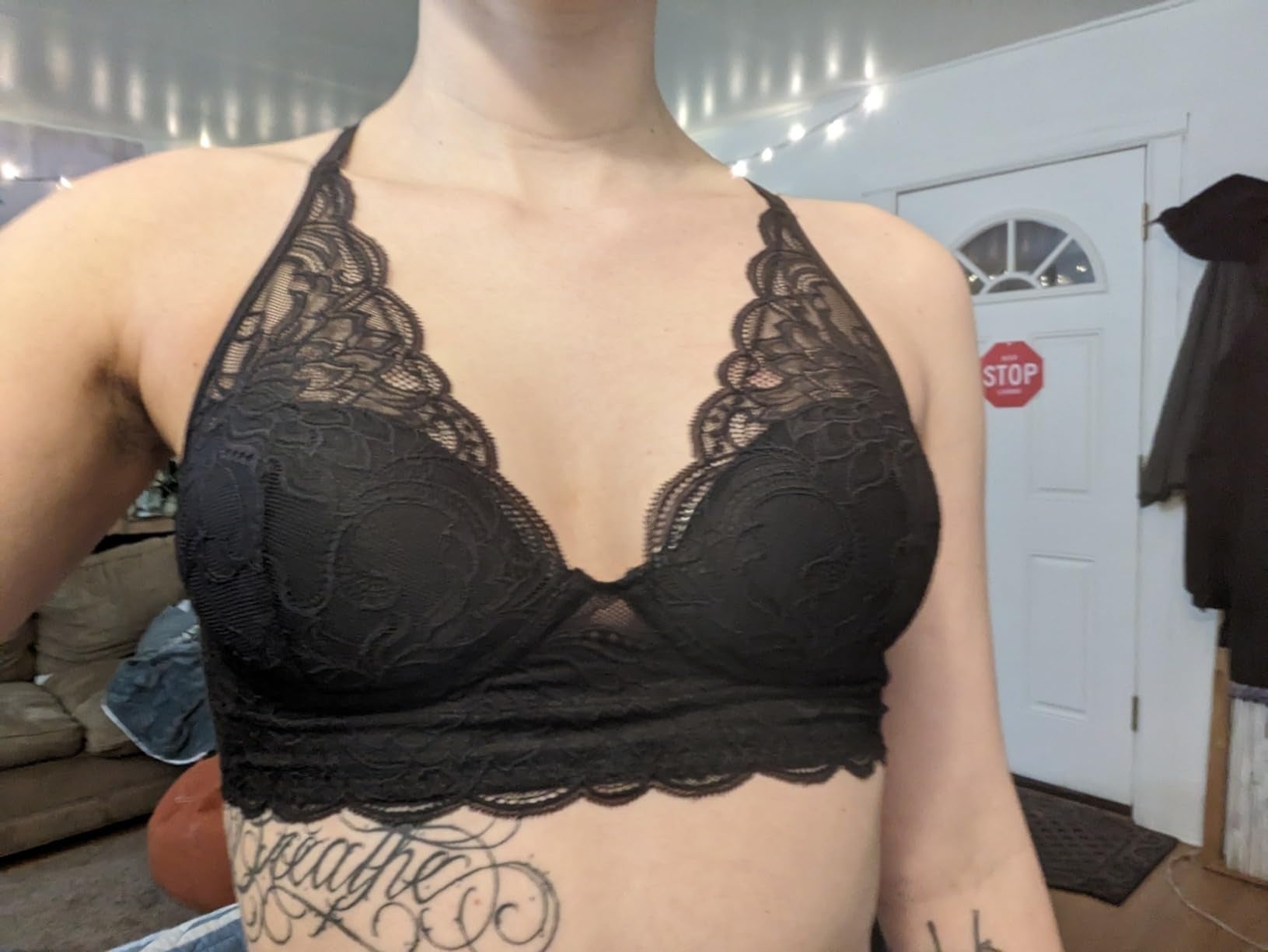 Person wearing a achromatic  lace bralette with scalloped edges, successful  a location  mounting  with a sofa and disposable   halt  motion   connected  the doorway  successful  the background