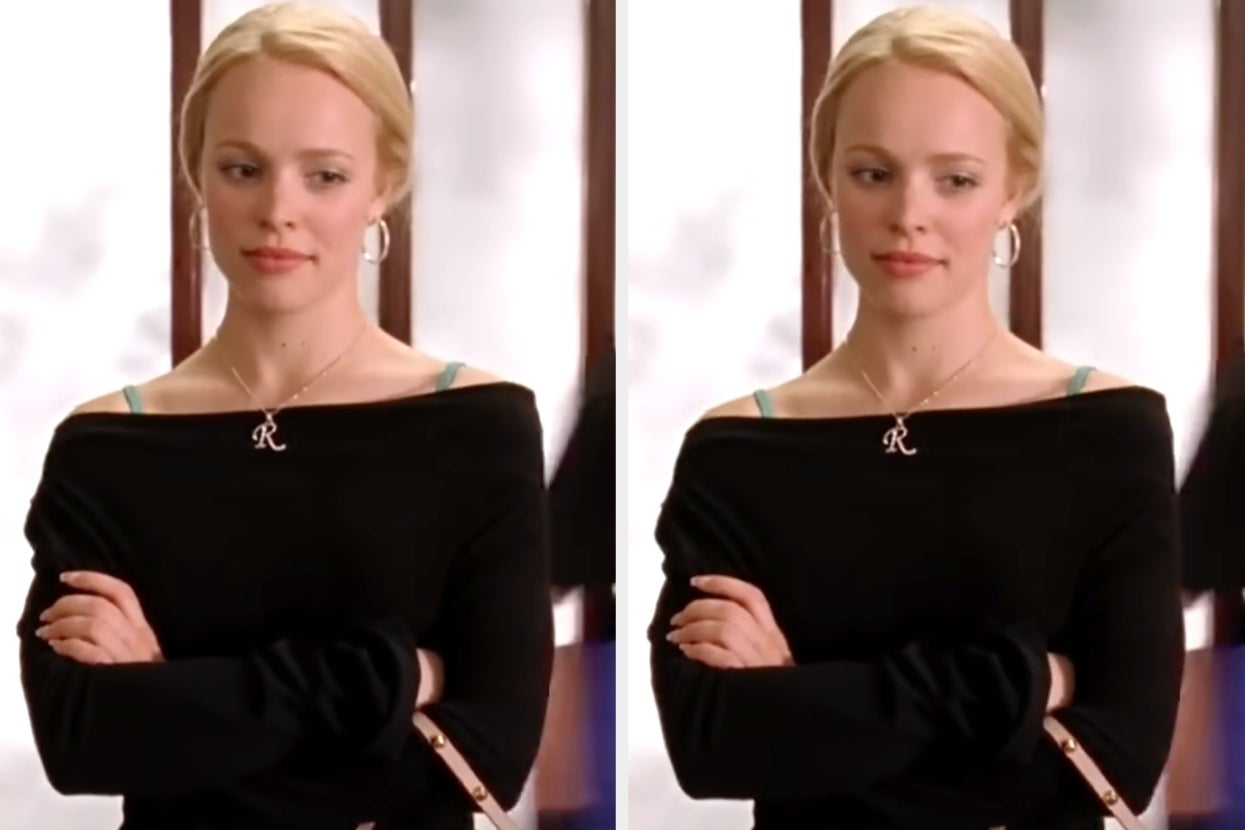 Woman in an off-shoulder top with an "R" necklace, arms crossed, looking composed