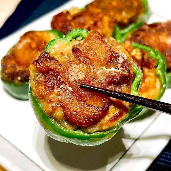 ピーマンと肉を使った料理が皿に盛られている。箸で料理を持ち上げている。