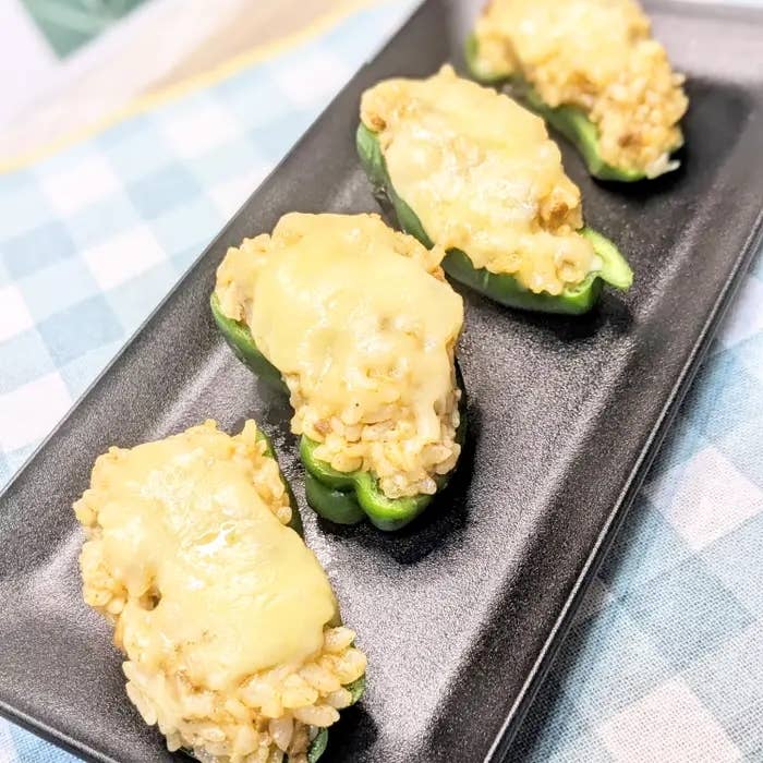 チーズとライスを詰めた4つの緑のピーマンが黒いプレートに並んでいる。背景は格子模様のテーブルクロス。