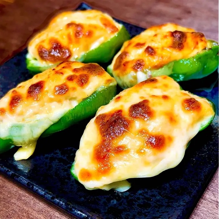 焼いたチーズがのったピーマンの詰め物料理が黒い皿に盛られている。