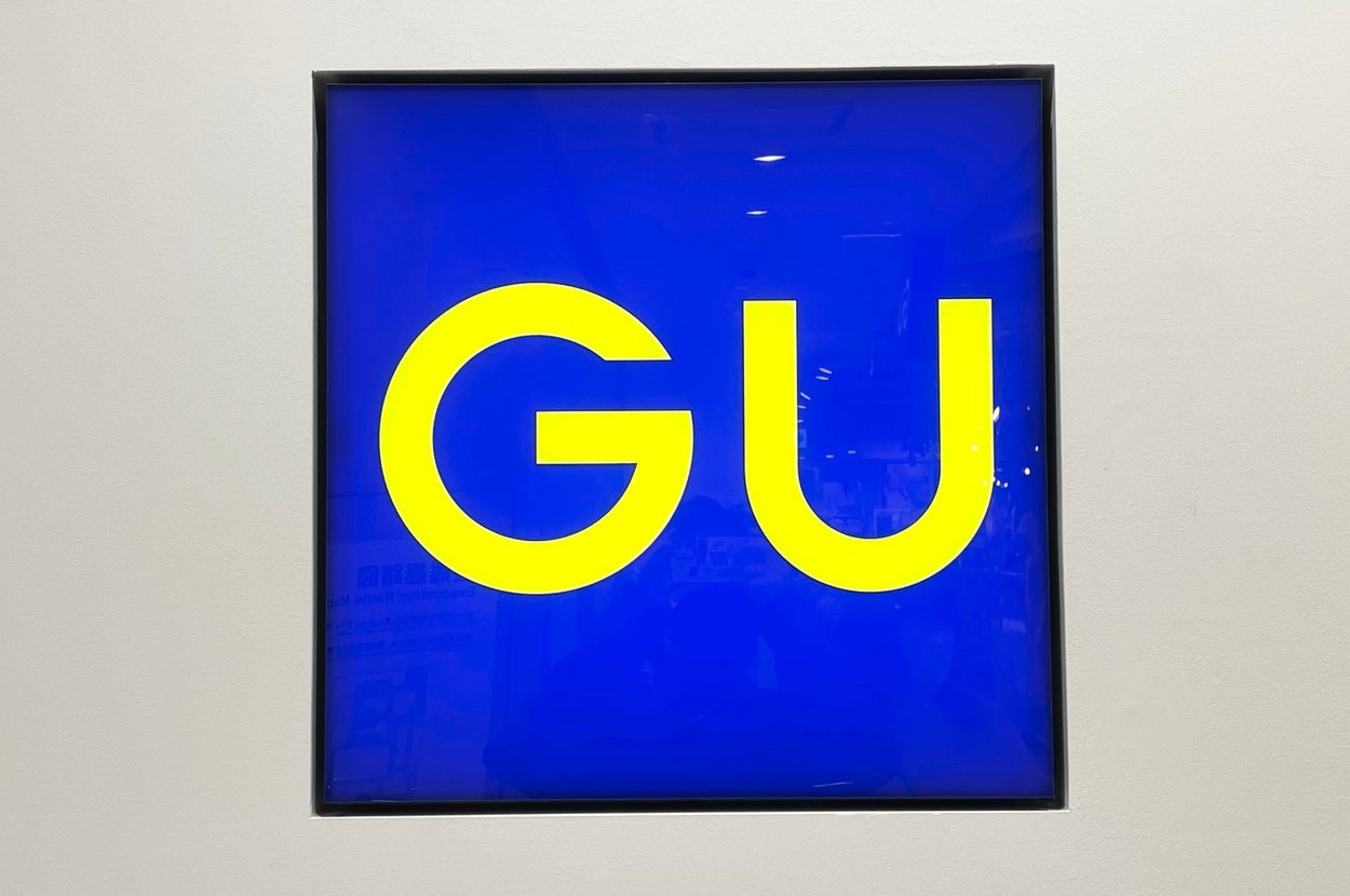 The image shows a sign with bold letters "GU" inside a square frame