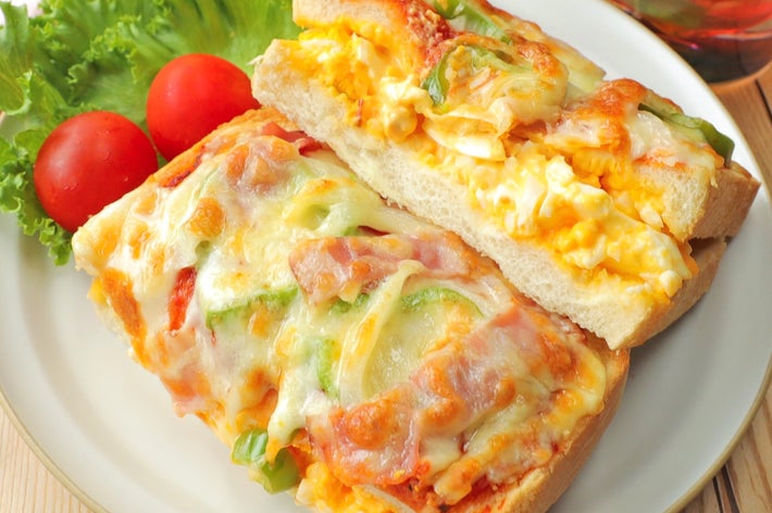 チーズと野菜がトッピングされたピザトーストが2枚、皿の上に載っている。隣にレタスとトマトが添えられている。