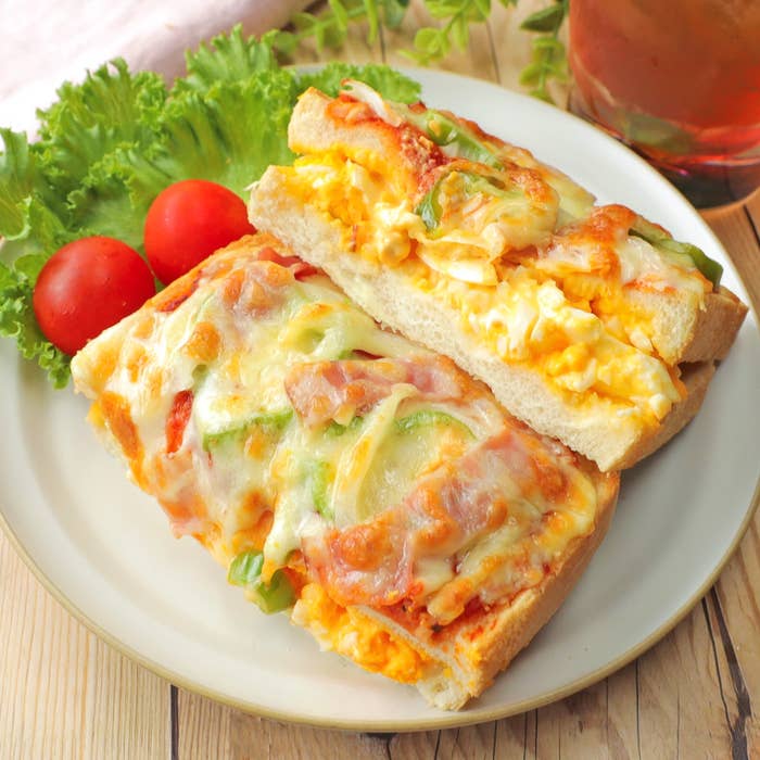 チーズと野菜がトッピングされたピザトーストが2枚、皿の上に載っている。隣にレタスとトマトが添えられている。