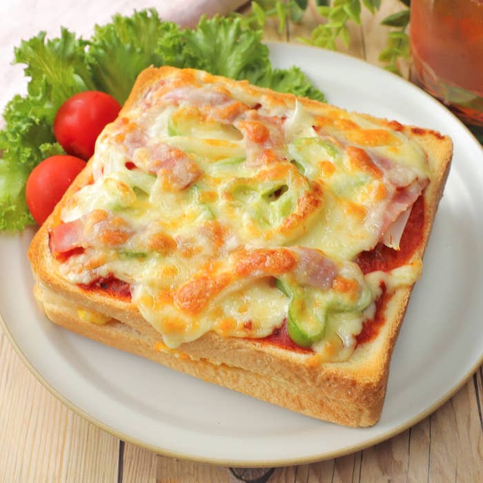 トーストの上にピザ風にチーズ、ベーコン、ピーマンが載っている料理。隣にレタスとミニトマトが添えられている。