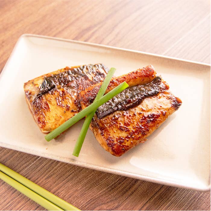 お皿に盛られた焼き魚の切り身2つと青いネギが添えられています。