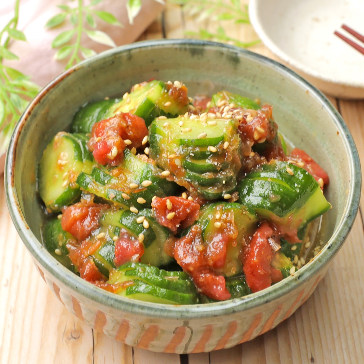 ゴマとトマトを添えたキュウリの和え物が器に盛られている。シンプルで美味しそうな野菜料理。